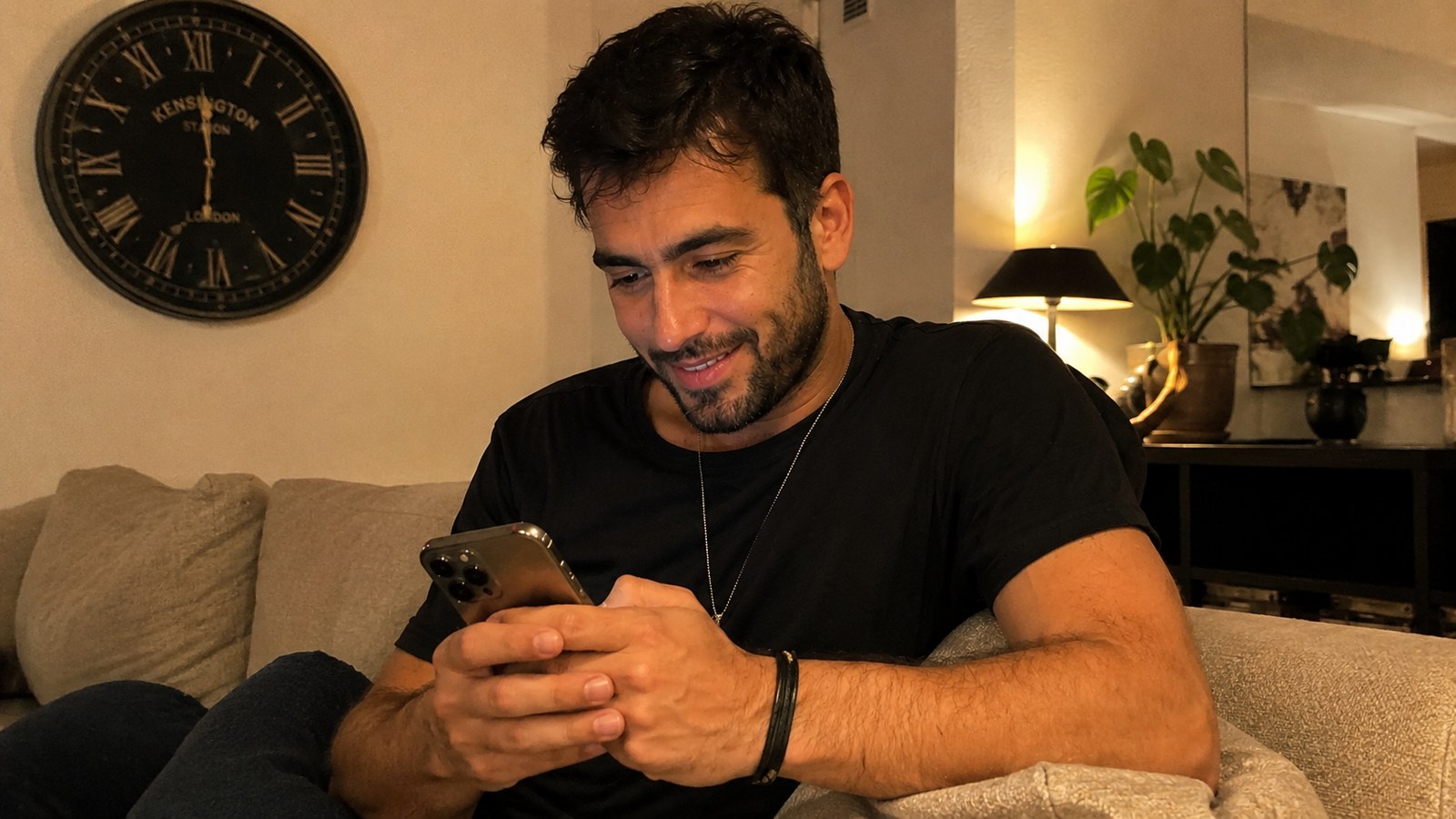 A relaxed man at home on a Sunday evening checking his phone, wall clock behind him