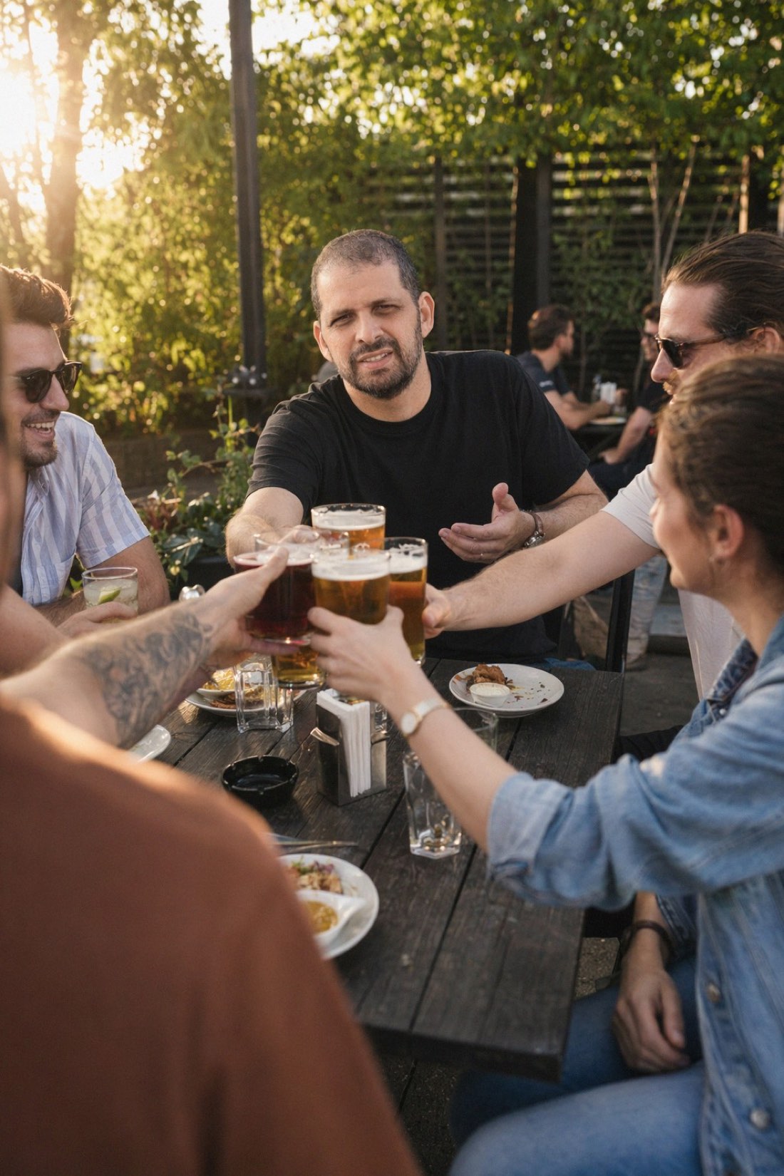 Man raising glasses with friends at a golden-hour beer garden