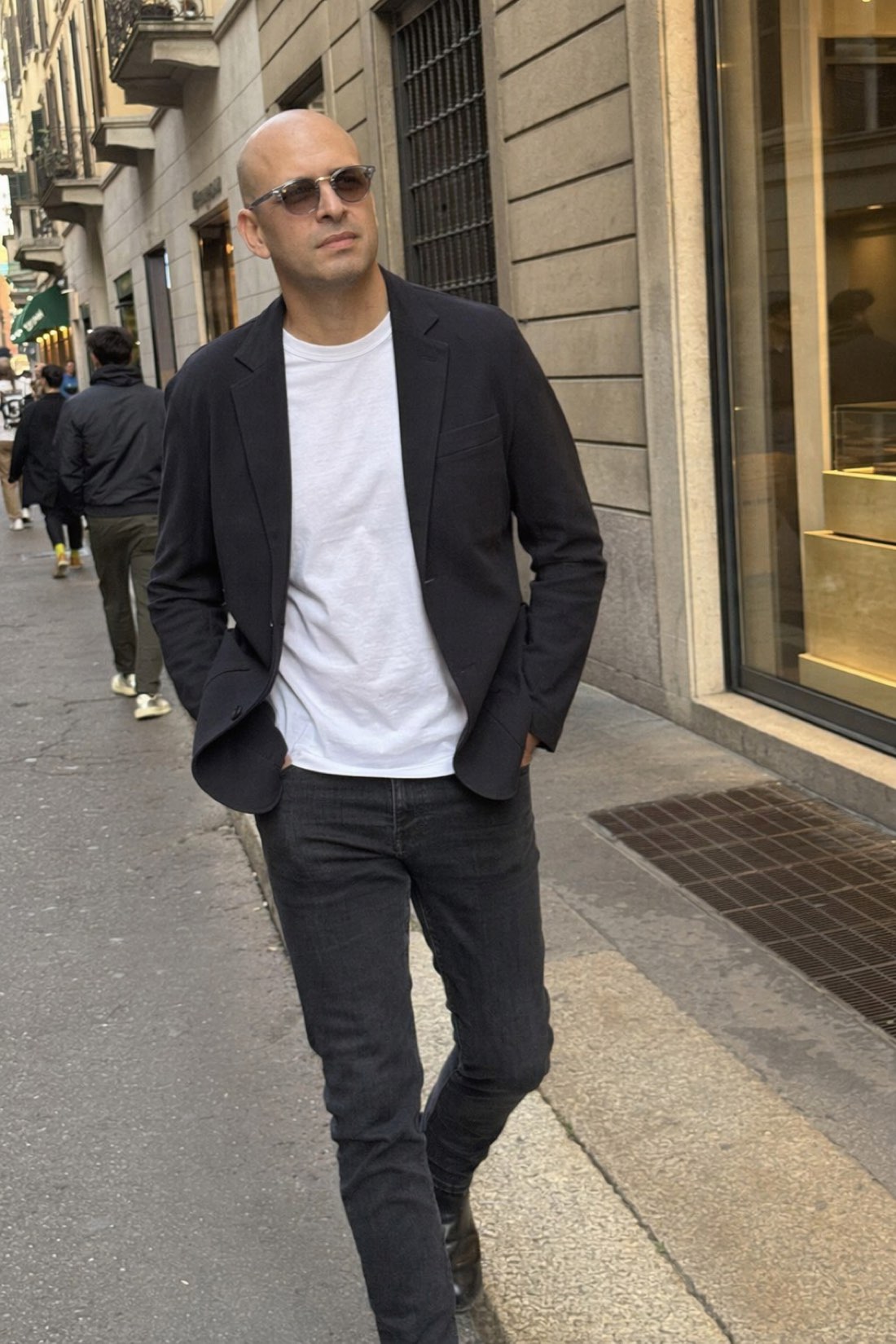 Man in an unstructured black blazer over a white tee walking a city street