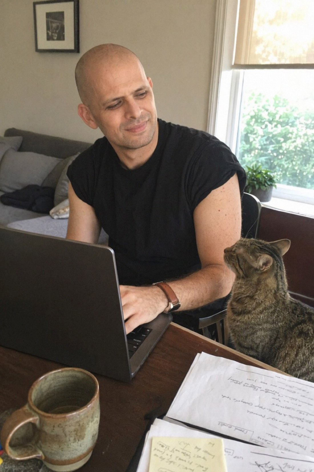 Man working on a laptop at home while a tabby cat supervises
