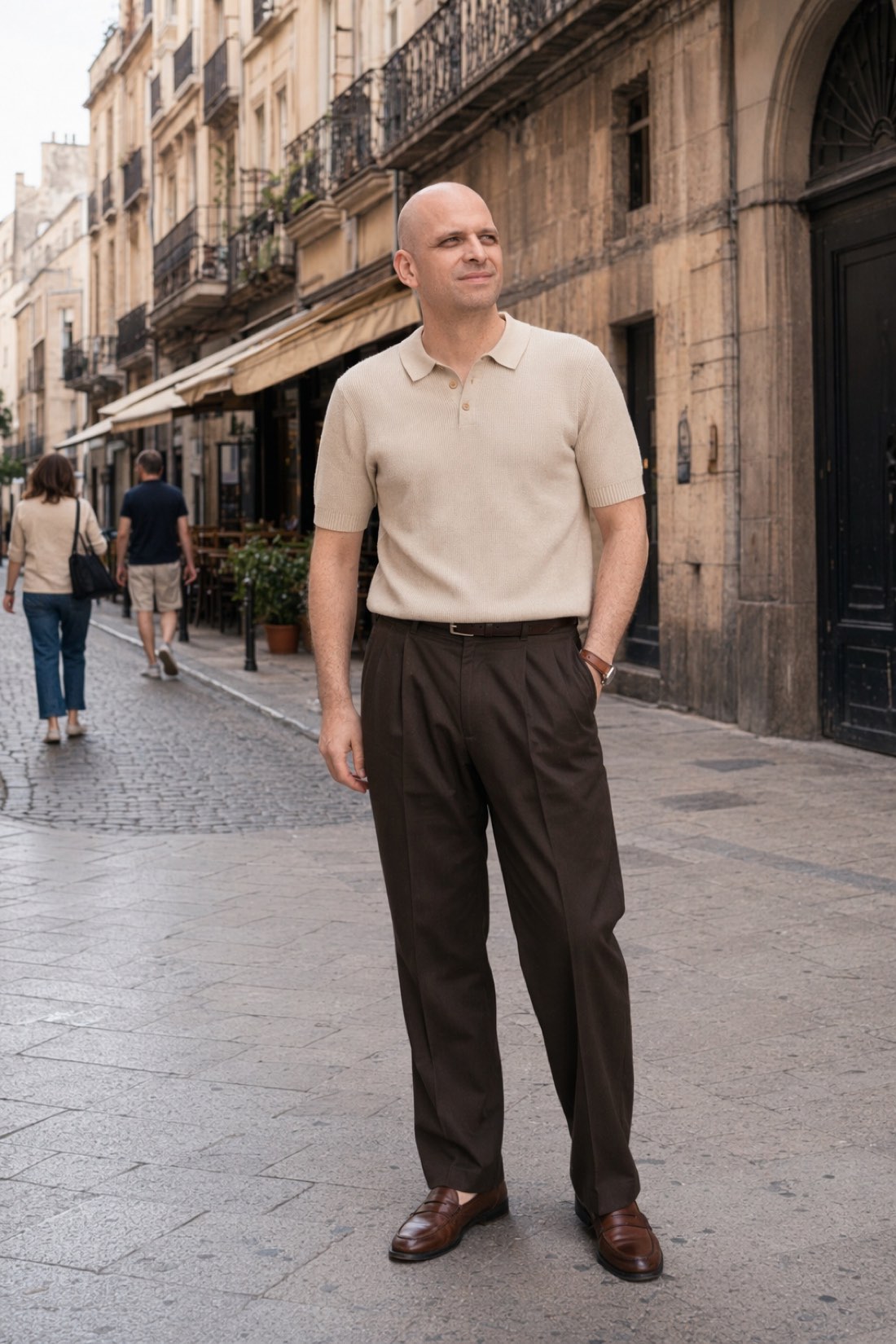 Man in a cream knitted polo and brown trousers on a city street