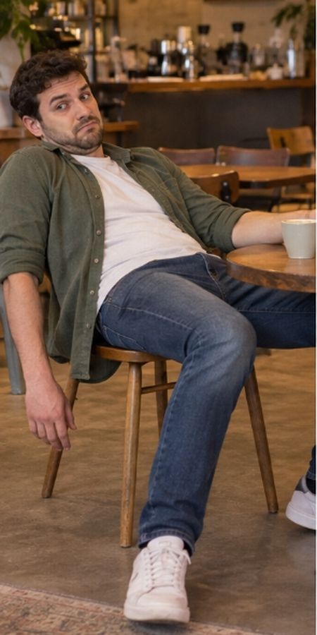 A man slumped far back in a cafe chair, legs sprawled out, one arm hanging dead off the side