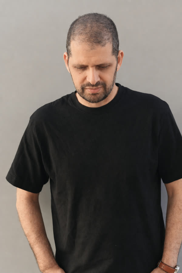 Reference photo: the same man, head lowered, plain wall behind him
